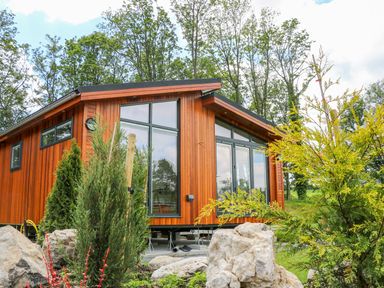 A wooden house with large windows surrounded by rocks and trees at Robin Lodge in Gargrave