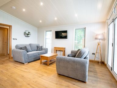 A living room with two grey sofas a coffee table a wall mounted tv and a floor lamp at Bluebell Lodge in Gargrave