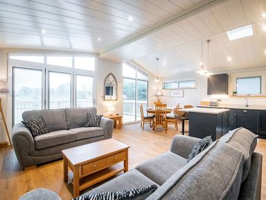 An open living space with two gray sofas a wooden coffee table dining table with chairs kitchen area with island and pendant lights at Bluebell Lodge in Gargrave
