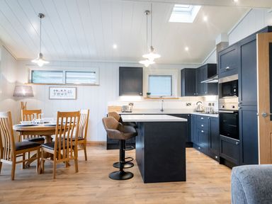 A kitchen and dining area with wooden dining chairs and a table next to a kitchen island with bar stools at Bluebell Lodge in Gargrave
