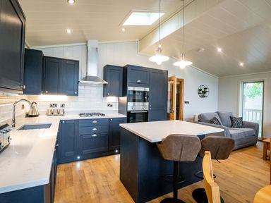 A kitchen and living area with blue cabinets a white island two bar stools a gray sofa and wooden flooring at Bluebell Lodge in Gargrave