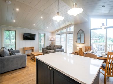 An open-plan room with a kitchen island, sofas, a dining table, and large windows at Bluebell Lodge in Gargrave