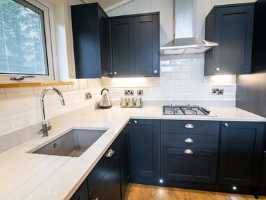 A kitchen with dark cabinets a white countertop a sink a gas stove and a stainless steel kettle at Bluebell Lodge in Gargrave