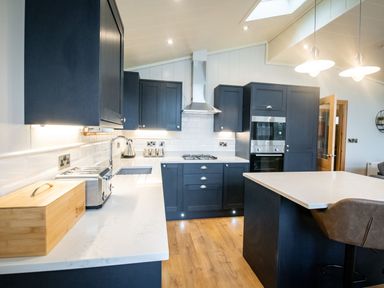 A kitchen with blue cabinets white countertops a gas stove an oven a toaster and a wooden bread box at Bluebell Lodge in Gargrave