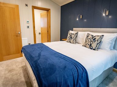 A bedroom with a bed white linens blue blanket and patterned cushions at Bluebell Lodge in Gargrave