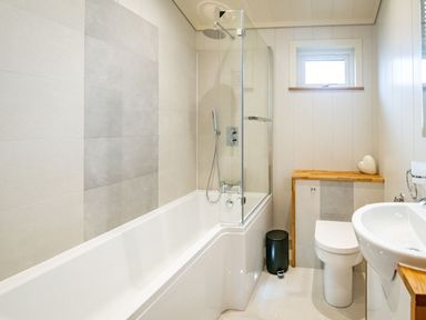A bathroom with a bathtub a shower a toilet a sink a small window and a black trash bin at Bluebell Lodge in Gargrave