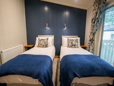 A bedroom with two single beds with blue blankets and patterned cushions at Bluebell Lodge in Gargrave