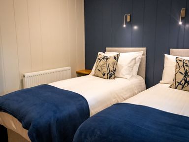 A bedroom with two single beds with blue blankets and patterned pillows at Bluebell Lodge in Gargrave