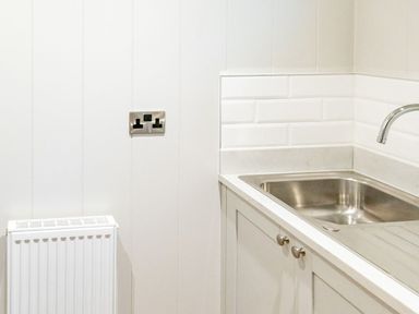 A kitchen corner with a stainless steel sink a faucet white cabinets a radiator and a double power socket on the wall at Bluebell Lodge in Gargrave