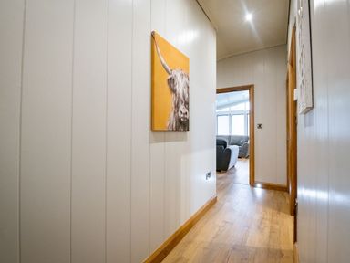 A hallway with wood flooring a painting of an animal on the wall and a view of a living room with sofas at Bluebell Lodge in Gargrave