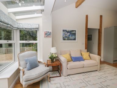 A living room with a beige sofa yellow and blue pillows a light blue cushioned armchair wooden side table with flowers and a lamp at The Roost in Cheriton near Alresford