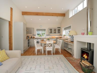 A kitchen and dining area with a round table and chairs next to a wood burning stove at The Roost in Cheriton near Alresford