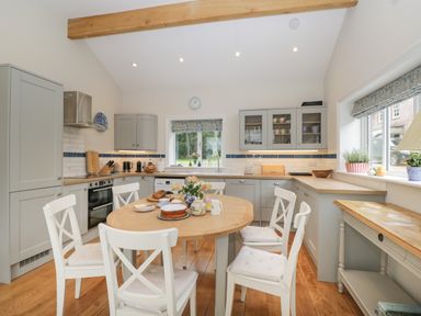A kitchen with wooden dining table and white chairs with cabinets and a window at The Roost in Cheriton near Alresford