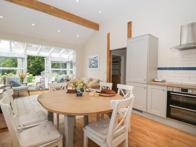 A kitchen with wooden dining table and white chairs next to a seating area with armchairs and a sofa at The Roost in Cheriton near Alresford