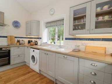 A kitchen with light grey cabinets a washing machine a double sink and glass cabinet at The Roost in Cheriton near Alresford