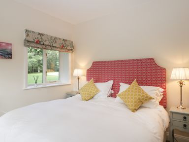 A bedroom with a bed with red patterned headboard yellow pillows bedside tables with lamps and a window with floral curtain at The Roost in Cheriton near Alresford
