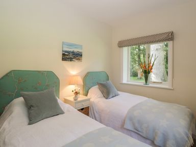 A bedroom with two single beds a nightstand with lamp and window with flowers at The Roost in Cheriton near Alresford