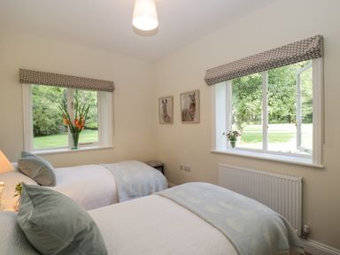 A bedroom with two single beds, pillows, blankets, two windows with floral curtains, flowers on windowsills and animal pictures on the wall at The Roost in Cheriton near Alresford