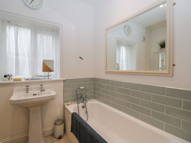 A bathroom with a white bathtub and sink a large mirror and a window with sheer curtains at The Roost in Cheriton near Alresford