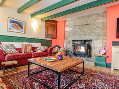 A living room with a red sofa colorful cushions a wooden coffee table a rug and a stone fireplace at Trewenna Roseland Tregony