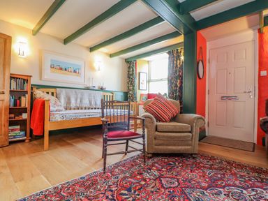 A living room with an armchair and wooden chair on a patterned rug and a sofa with books on shelves at Trewenna Roseland Tregony