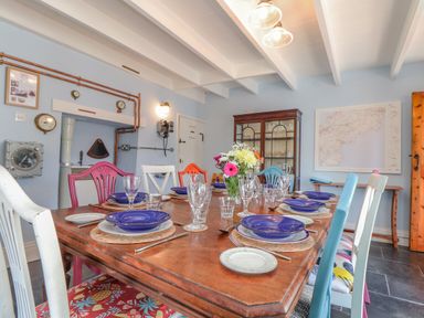 A dining room with a wooden table set with blue plates and glasses and a vase of flowers at Trewenna Roseland Tregony