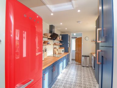 A kitchen with a red fridge blue cabinets wooden countertops and patterned floor tiles at Trewenna Roseland Tregony