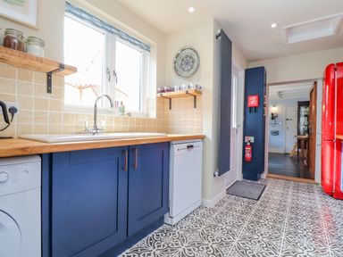 A kitchen with blue cabinets wooden countertop a sink dishwasher patterned floor and red fridge at Trewenna Roseland Tregony