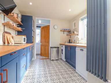 A kitchen with blue cabinets wooden countertops patterned floor tiles and a wooden door at Trewenna Roseland Tregony