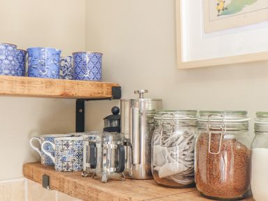 A kitchen shelf with blue patterned mugs glass jars containing tea bags and instant coffee at Trewenna Roseland Tregony