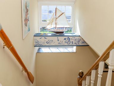 A stairwell window with a model sailboat and painted blue and white floral designs at Trewenna Roseland Tregony