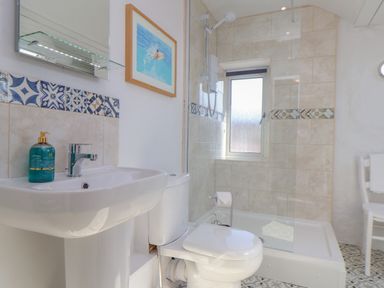 A bathroom with a sink soap dispenser toilet shower area and a window at Trewenna Roseland Tregony