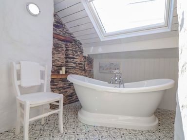 A bathroom with a white freestanding bathtub a white chair with a towel and patterned floor tiles at Trewenna Roseland Tregony