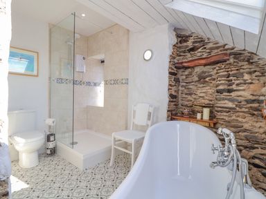 A bathroom with a toilet, glass shower, white chair, bathtub, and stone wall at Trewenna Roseland Tregony