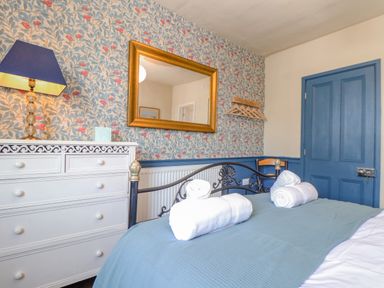 A bedroom with a wrought iron bed a white chest of drawers a blue door and floral wallpaper at Trewenna Roseland Tregony