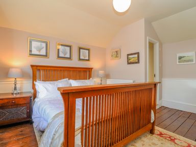 A bedroom with a wooden bed frame white bedding bedside tables with lamps and paintings on the walls at Trewenna in Roseland Tregony