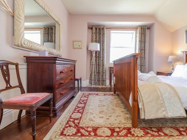 A bedroom with a wooden bed bedspread rolled towels a wooden dresser chair floral curtains and a floor lamp at Trewenna in Roseland Tregony