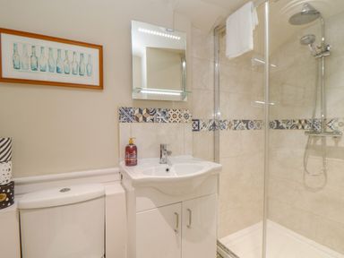 A bathroom with a shower area, a sink with cabinet, a toilet, and a framed picture of bottles on the wall at Trewenna Roseland Tregony