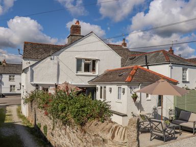 A white house with a patio area and outdoor furniture including an umbrella and seating at Trewenna Roseland Tregony