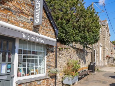 A stone building with a gallery sign and a large window next to a stone wall with plants and a bench at Trewenna Roseland Tregony