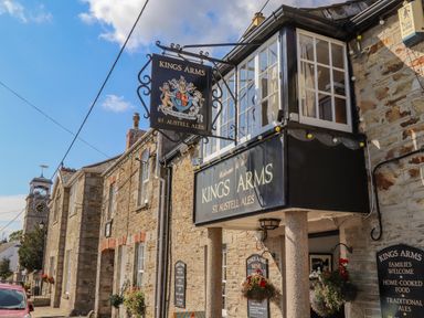 The exterior of a stone building with signs for Kings Arms pub and hanging flower baskets in a street at Trewenna Roseland Tregony