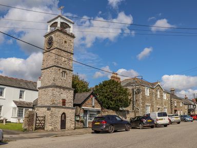 A street with a stone clock tower cars parked and historic buildings at Trewenna Roseland Tregony