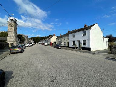 A street view with parked cars a clock tower on the left and houses on the right at Trewenna Roseland Tregony