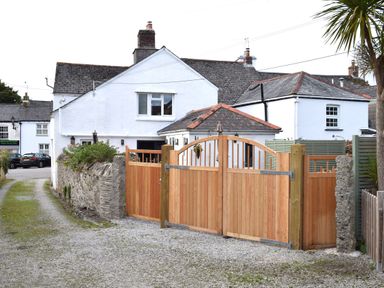 A white house with a gravel driveway and wooden gates at Trewenna in Roseland Tregony