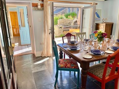 A dining area with a wooden table set for six with assorted chairs and flowers at Trewenna Roseland Tregony