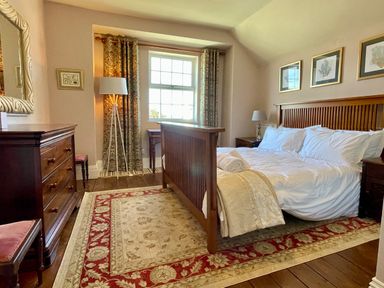 A bedroom with a wooden bed a dresser a table lamp and framed art on the walls at Trewenna in Roseland Tregony