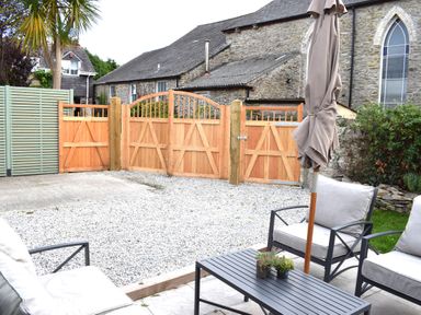 A patio with outdoor chairs and table with a closed umbrella and a wooden fence in the background at Trewenna Roseland Tregony