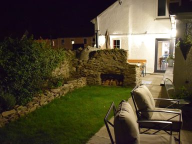 A backyard with stone wall and grass with outdoor chairs and a white house in the background at Trewenna Roseland Tregony