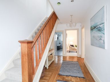 A hallway with wooden stairs carpeted floor and a painting on the wall at Awelfryn in Criccieth