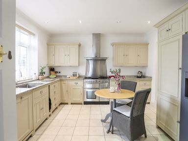 A kitchen with beige cabinets a stainless steel stove a round wooden table with two chairs and a window at Awelfryn in Criccieth